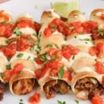 Front angle view on a few vegan taquitos on a plate covered with a cashew cheese sauce and salsa.