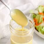 There is a spoon drizzling a vegan honey mustard dressing in a jar.