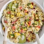 View on a large serving bowl of a cilantro lime pasta salad with 2 large serving spoon.