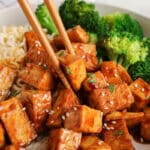 Chopsticks taking a pieces of hoisin tofu from a bowl.