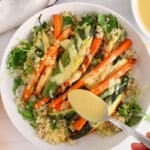 There is a spoon adding more sunshine dressing over roasted vegetables on a plate.
