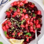 View on a bowl of a beet watermelon salad with basil and lemon wedges on the side.