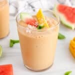 View on a glass of watermelon mango smoothie garnished with fresh fruit and shredded coconut.