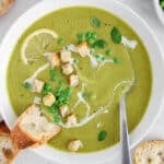 View on a bowl of broccoli pea soup garnished with crouton with a side of bread.