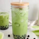 Showing a tall glass of honeydew bubble tea with a glass of vegan milk and pieces of honeydew melon in the background.
