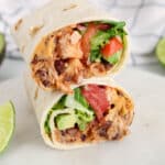 View on 2 halves jackfruit wraps over each other filled with a jackfruit black bean creamy mixture, lettuce, tomatoes and a chipotle sauce.