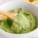 View on a bowl with some vegan cashew basil pesto and a wooden spoon that's stirring.