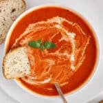 Overhead view on a bowl of creamy dairy-free tomato soup with a drizzle of coconut milk over and fresh basil.