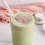 Front angle view on a tall glass of strawberry matcha smoothie dusted with matcha powder.