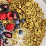 Close up on the green granola from a bowl with berries and oat milk.