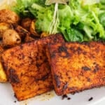 View on a plate made out of vegan blackened tofu steaks with crispy potatoes and a salad.