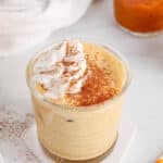 Showing is a short glass filled with a vegan creamy pumpkin spiced milk topped with oat whipped cream and spices.