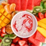 Overhead view on a large platter of fresh fruit with a bowl of vegan fruit dip.