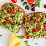 View on a plate with Mediterranean avocado toast with more olives and tomatoes on the side.