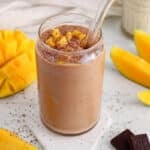Front angle view on a creamy dairy-free chocolate mango smoothie garnished with mango and shaved chocolate.