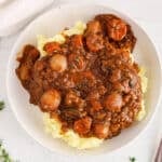 There is a vegan coq au vin over mashed potatoes on a plate.