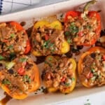 View on a large baking dish filled with 6 halved barley stuffed peppers made with also mushrooms, tomatoes and white beans.