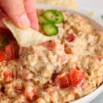 Close up on a tortilla chips taking some vegan Rotel dip from a bowl.