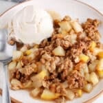 View on a plate with a vegan pear crumble with vanilla ice cream with a focus on the cubed soft cooked pear.