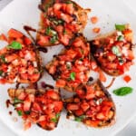 View on a plate with a few slices of vegan tomato bruschetta with a drizzle of balsamic glaze.
