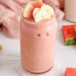Showing a tall glass of frosty watermelon banana smoothie.