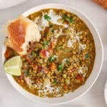 Overhead view on a bowl of coconut mung bean curry garnished with cilantro and a side of crusty baguette.