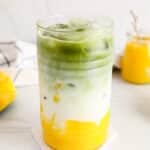 Showing a tall glass of a vegan mango matcha latte.