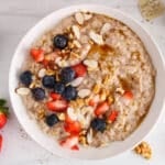 Showing is a bowl of creamy oatmeal with flaxseed garnished with berries, almonds and maple syrup.