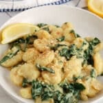View on a bowl of creamy kale gnocchi with a side of lemon wedge.
