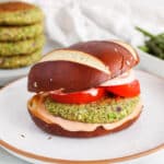 View on a vegan white bean broccoli burger on a plate with tomatoes and onion.