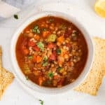 Overhead view on a bowl of lentil barley minestrone soup with a side of crackers.