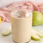View on a tall glass of a creamy banana pear smoothie topped with chia and cinnamon.