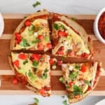 Overhead view on a vegan Mexican pizza sliced in quarters and topped with cheese sauce and salsa.