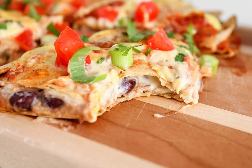 Close up on a slice of vegan Mexican pizza with a bite taken off showing the cheese bean filling.
