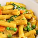 View on a bowl of pasta curry with peas, carrots and spinach.