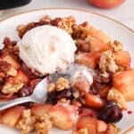 View on a plate with a portion of cherry apple crisp topped with vegan vanilla ice cream.