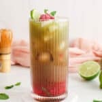 View on a layered raspberry matcha mocktail with fresh limes in the background.