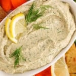 Overhead view on a bowl of lemon dill hummus with cucumber and crackers.