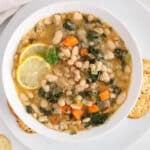 View on a bowl of lemony white bean soup with dill and kale with a side of crackers.