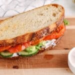 View on a vegan vegetable sandwich on a cutting board with roasted tomato, cucumber and avocado.