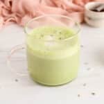 View on a mug of lavender matcha latte garnished with dried lavender buds and made with oat milk.