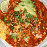 Close up on a creamy and vegan bowl of enchilada soup topped with avocado, chips, lime and cilantro.