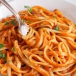 There is a fork taking a portion of linguini in a roasted tomato and pepper sauce.