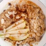 Close up on a bowl of spiced oatmeal garnished with slivered almonds and slices of pear.
