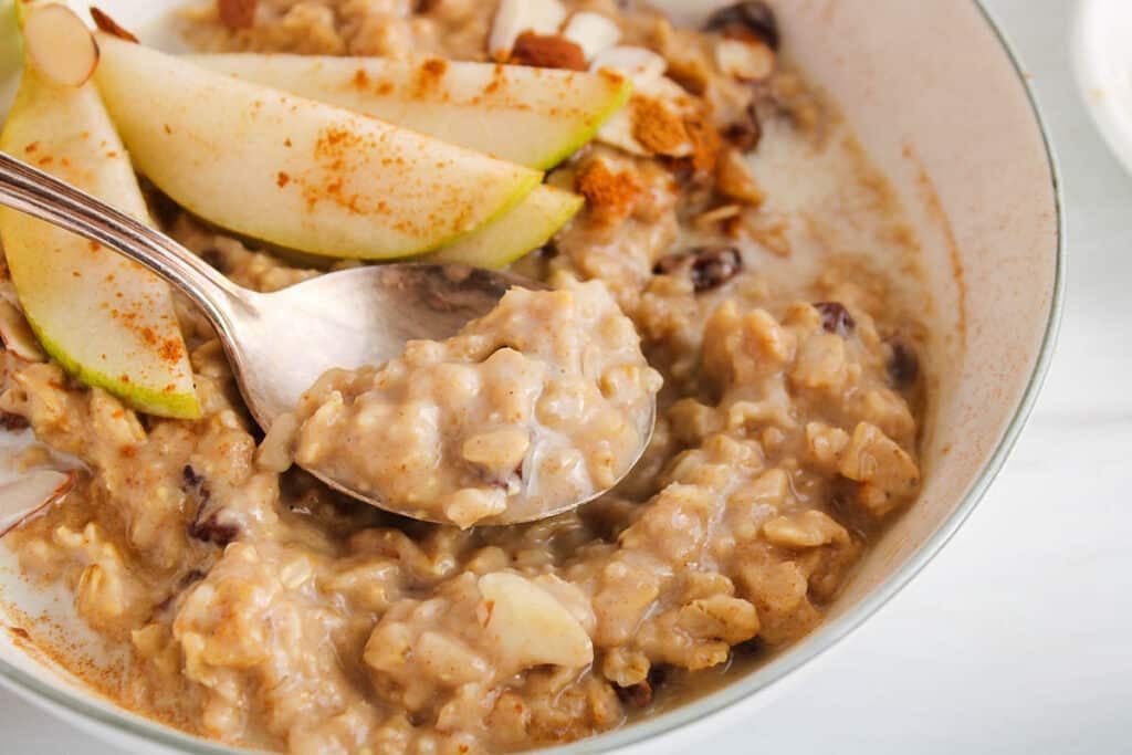 View on a spoon taking a bite of vegan creamy spiced oatmeal from a bowl.