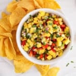 View on a bowl of mango corn salsa on a platter with tortilla chips.