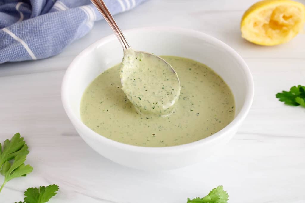 Close up on a spoon taking some lemon herb tahini dressing from a bowl to show the creamy texture.