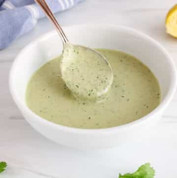 Close up on a spoon taking some lemon herb tahini dressing from a bowl to show the creamy texture.