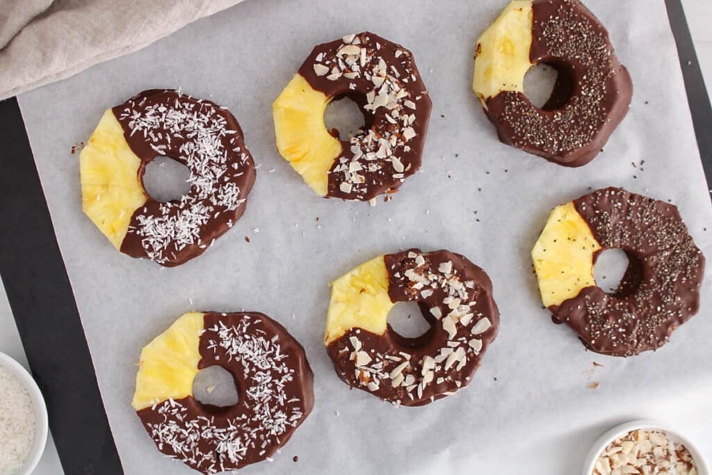 Overhead view on a few dark chocolate pineapple garnished with different ingredients.