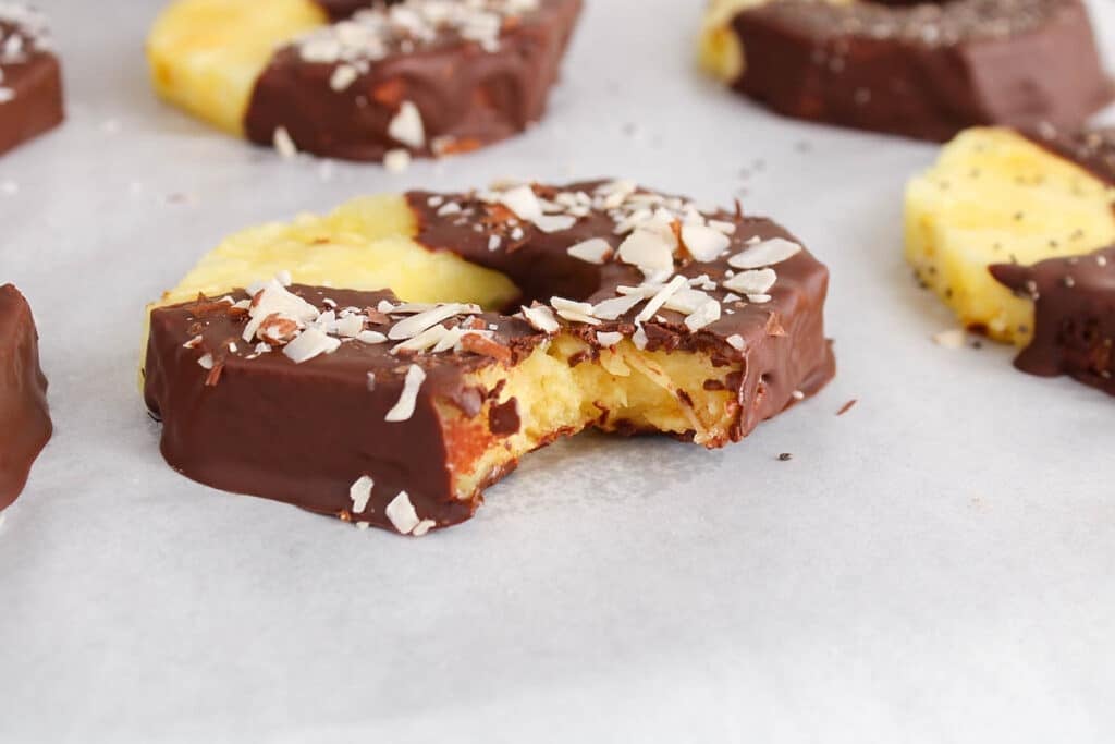 Close up on a chocolate covered pineapple with a bite taken off to show the middle fruit part.